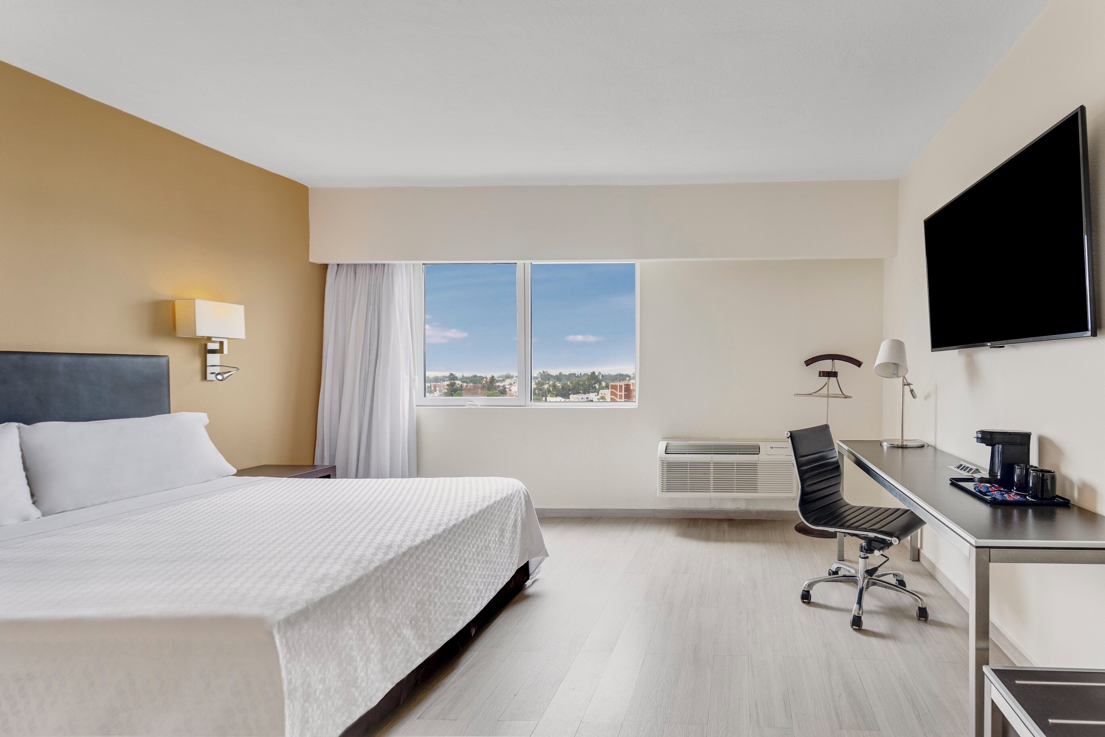 Habitación de hotel con cama, escritorio, silla, televisor y ventana con vista a la ciudad.