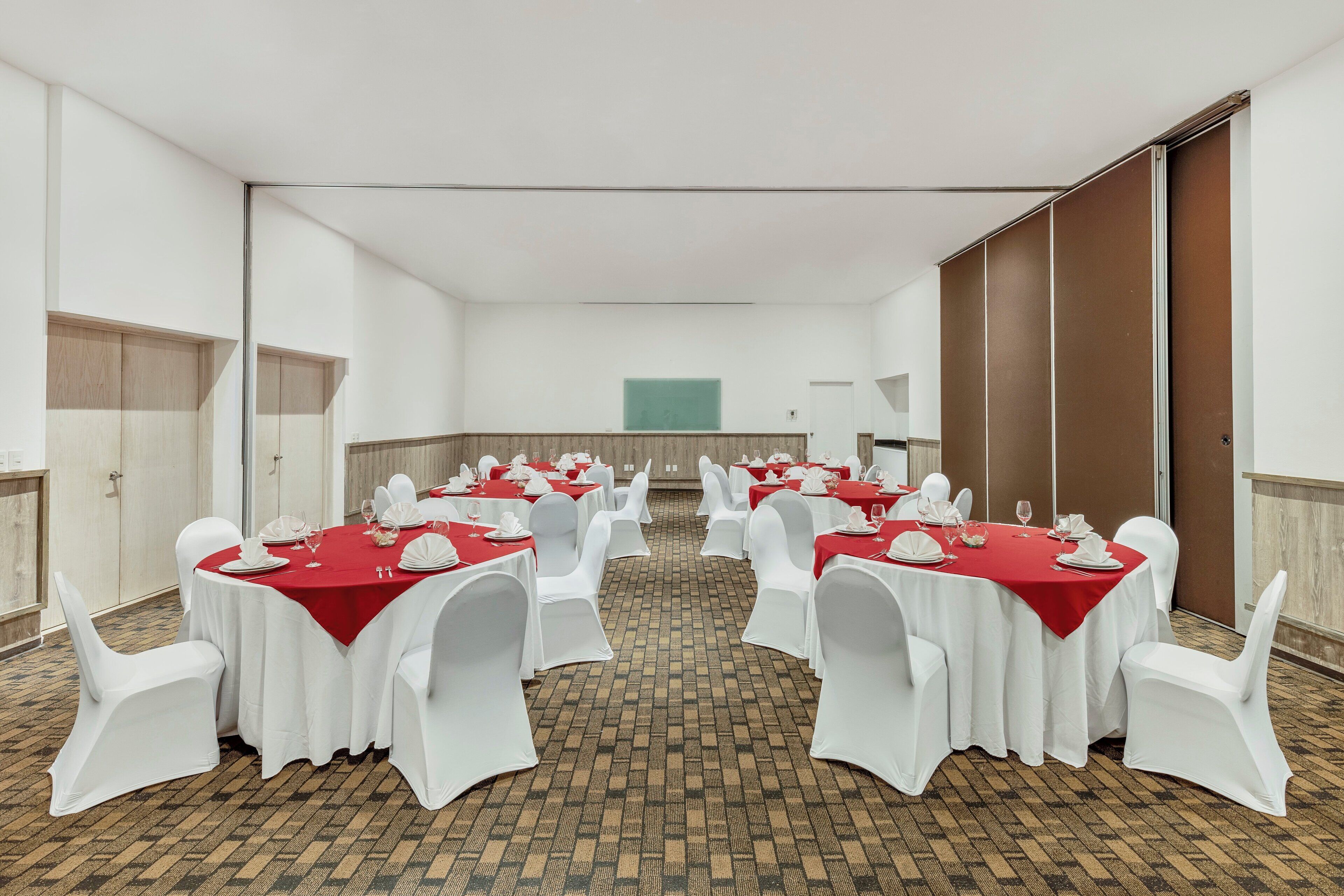 Une salle de conférence avec des tables rondes, des chaises blanches et des nappes rouges.