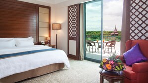 A hotel room with a large bed, a balcony with a view of a pagoda, and a table with fruit. - Hilton Mandalay (Mandalay)