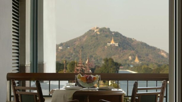 A balcony with a table set for two, overlooking a mountainous landscape with temples. - Hilton Mandalay (Mandalay)