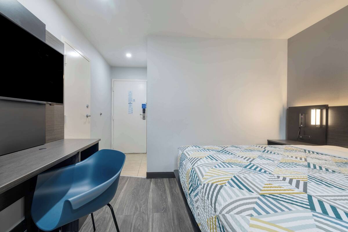 A hotel room with a bed, a desk, a chair, a TV, and a wardrobe.