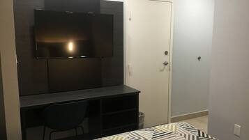Un dormitorio con cama, escritorio, silla, televisor montado en la pared y una puerta.