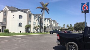 A motel with a parking lot, a black pickup truck, and a palm tree.