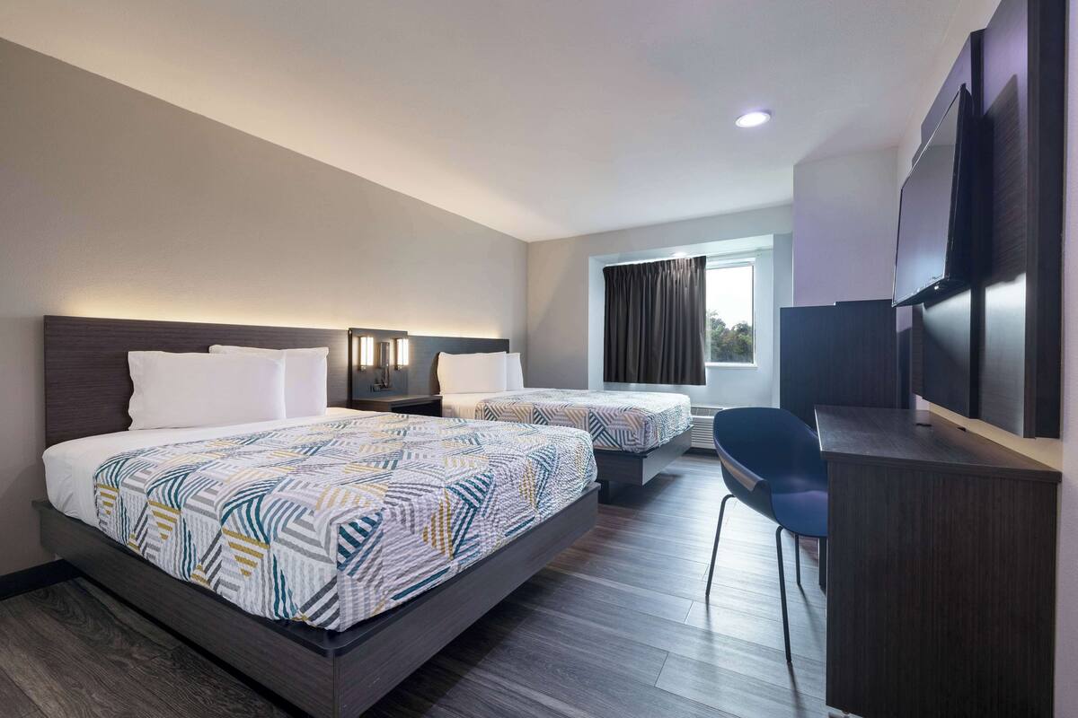 A hotel room with two beds, a desk, and a TV.