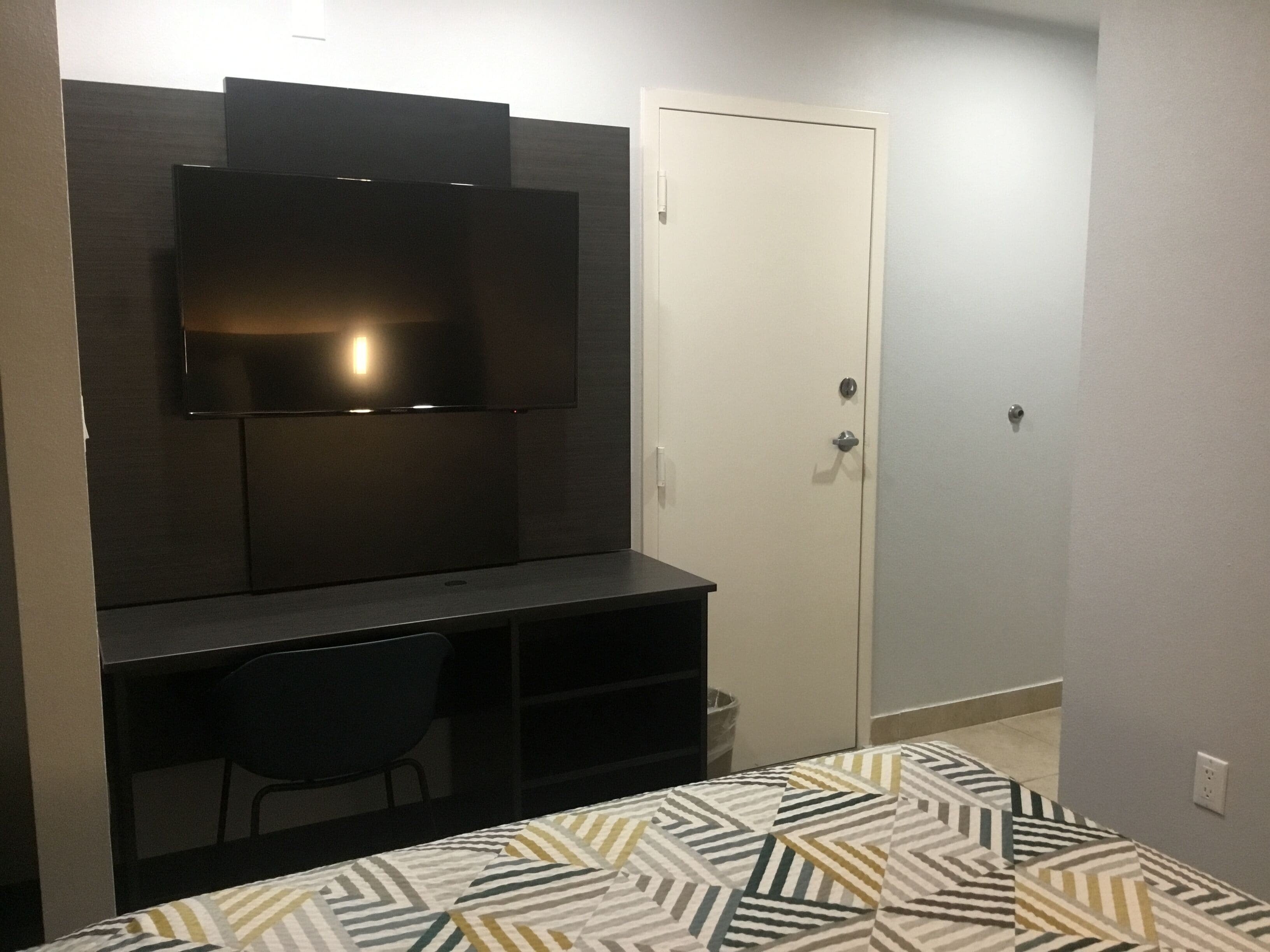 A compact bedroom with a bed, a desk, a chair, a television, and a wardrobe.
