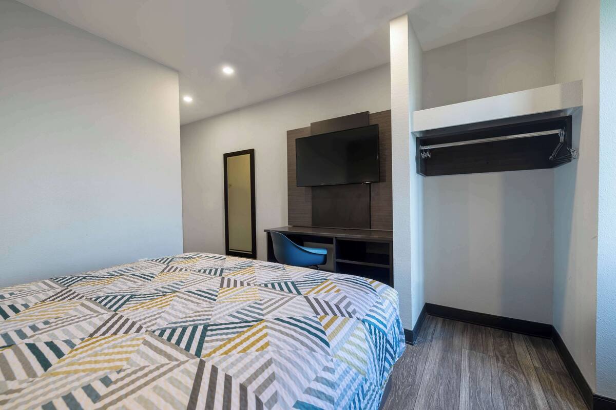 A hotel room with a bed, a desk, a chair, a TV, and a wardrobe.