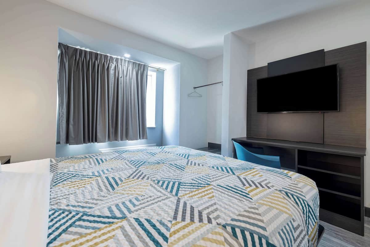 A modern hotel room with a large bed, a flat-screen TV mounted on a wooden panel, and a window with curtains.