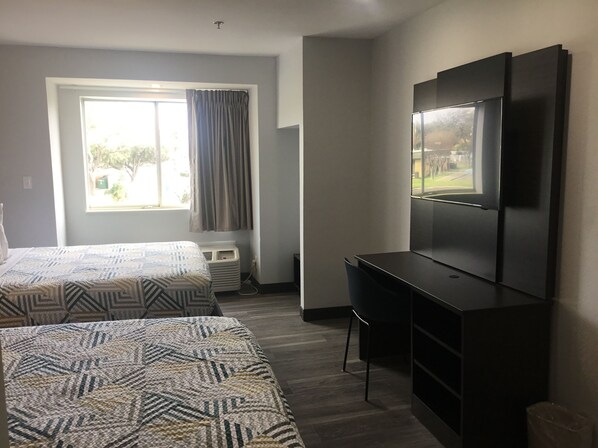 Habitación de hotel con dos camas, un escritorio, un televisor y una ventana con cortinas.