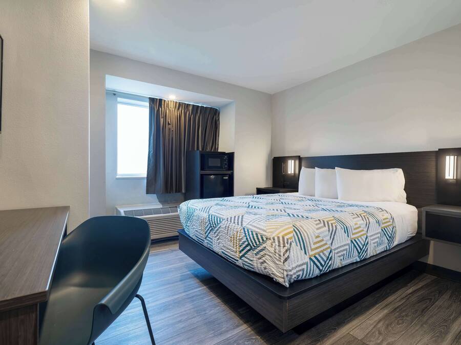 Camera d'albergo moderna con un ampio letto, una scrivania, una sedia, una televisione e una finestra con tende.