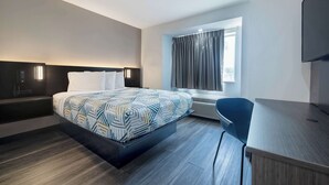 A modern hotel room with a large bed, a desk, a chair, and a TV.