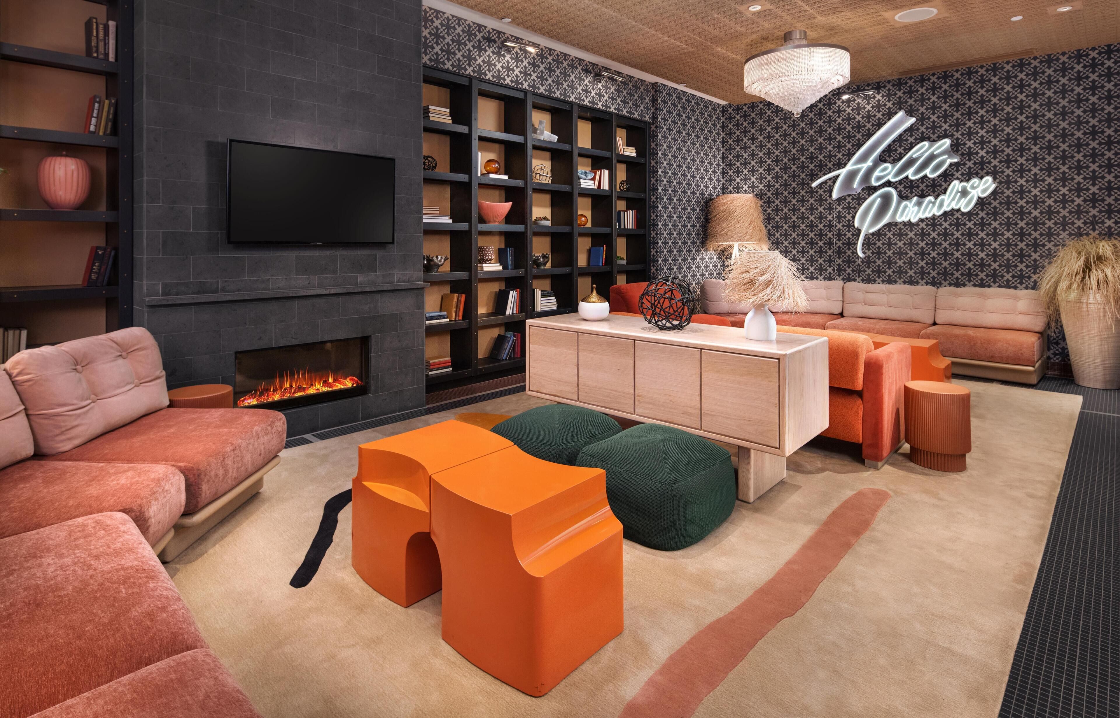 A modern living room with a fireplace, a large bookshelf, a sofa, and a 'Hello Paradise' sign on the wall.