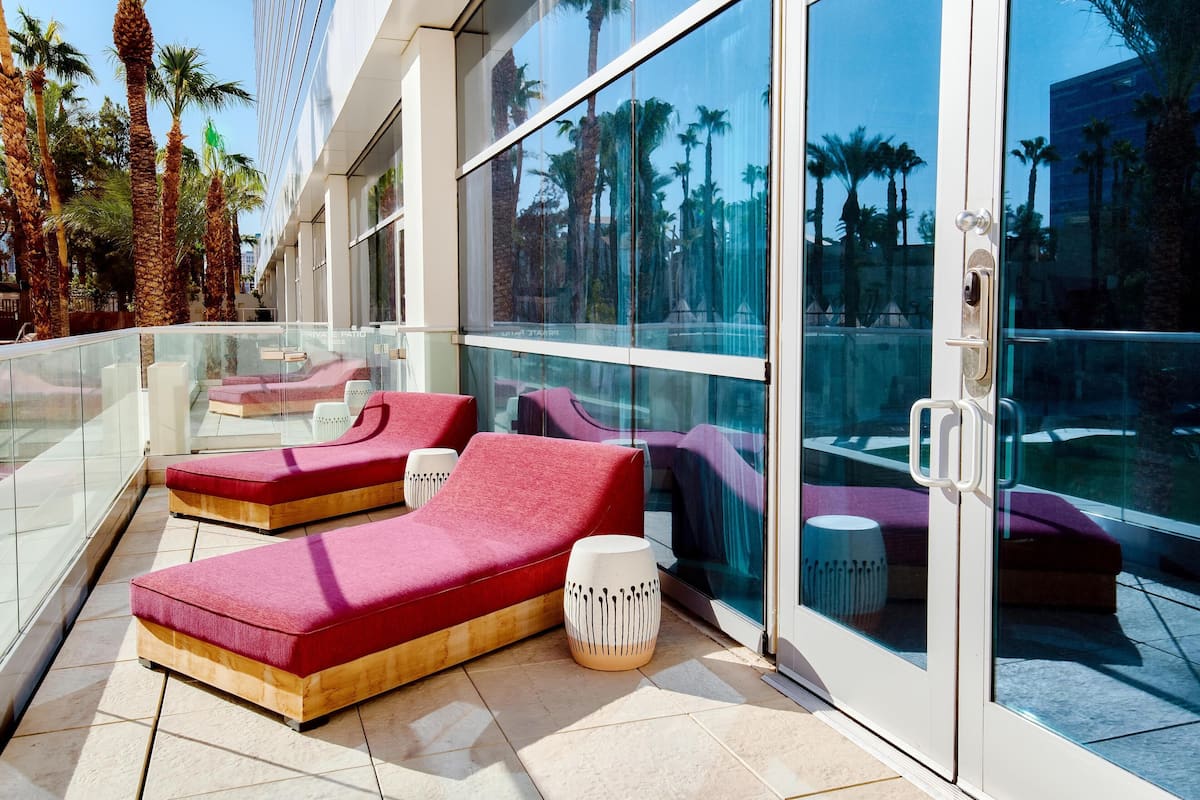 A modern outdoor lounge area with red and purple seating, glass walls, and palm trees in the background.