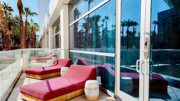 A modern outdoor lounge area with red and purple seating, glass walls, and palm trees in the background.