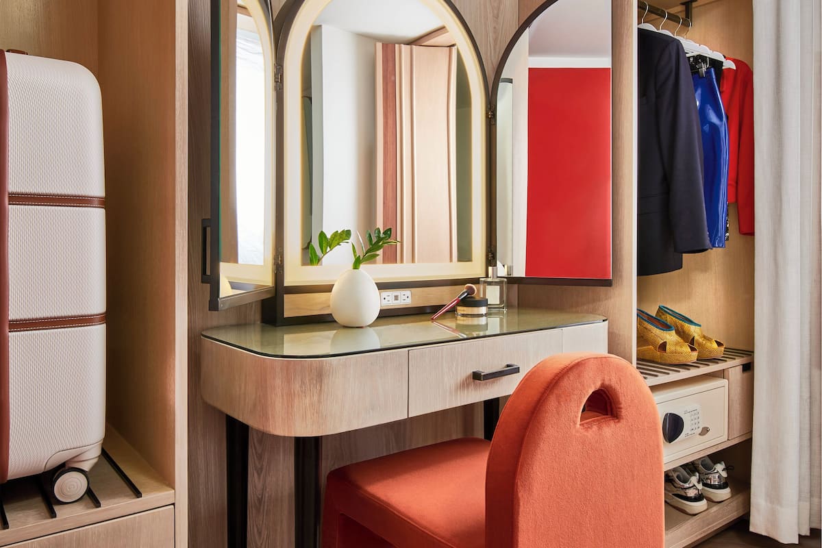 A compact bedroom with a wooden vanity, a mirror, a small plant, and a red chair.
