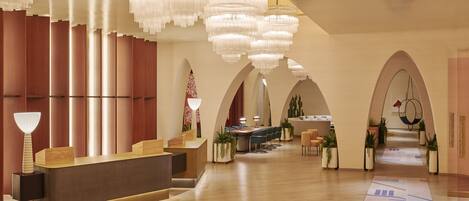 A hotel reception area with a modern design, featuring a reception desk, multiple seating areas, and decorative lighting.