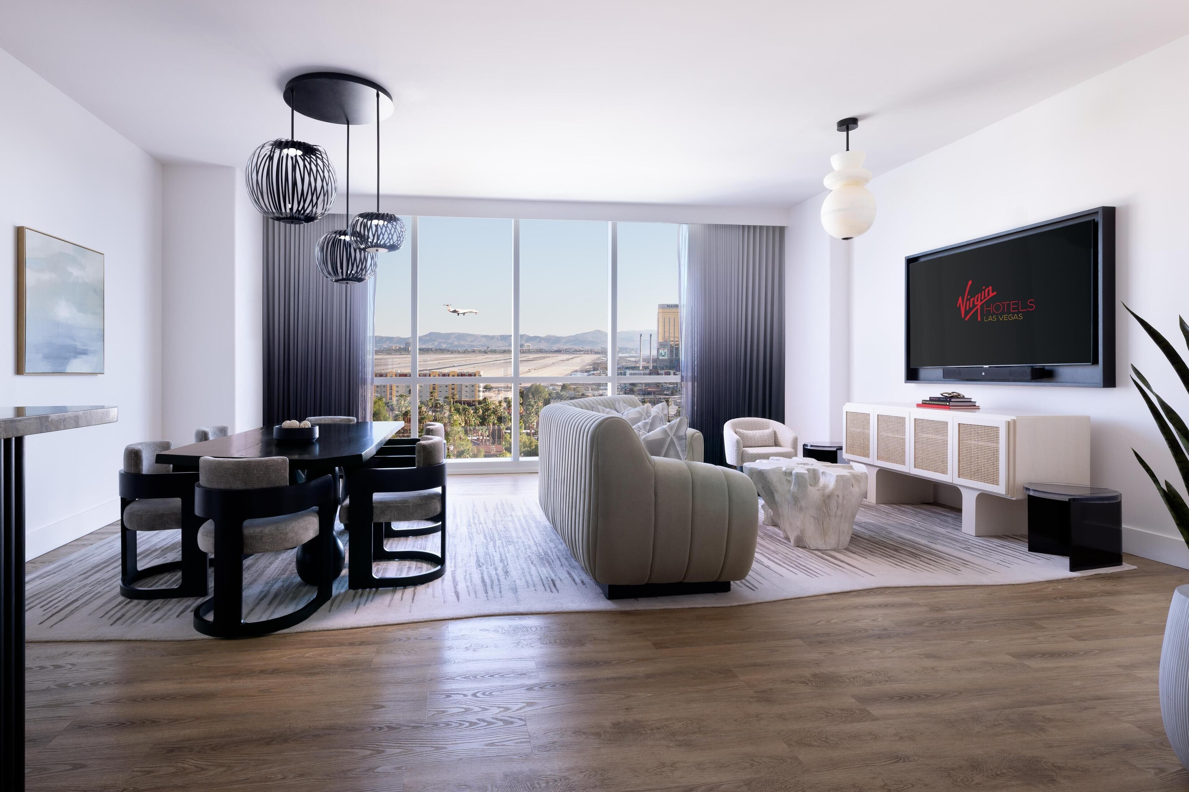 Uma sala de estar moderna com uma televisão grande, uma área de jantar e vista para a cidade.