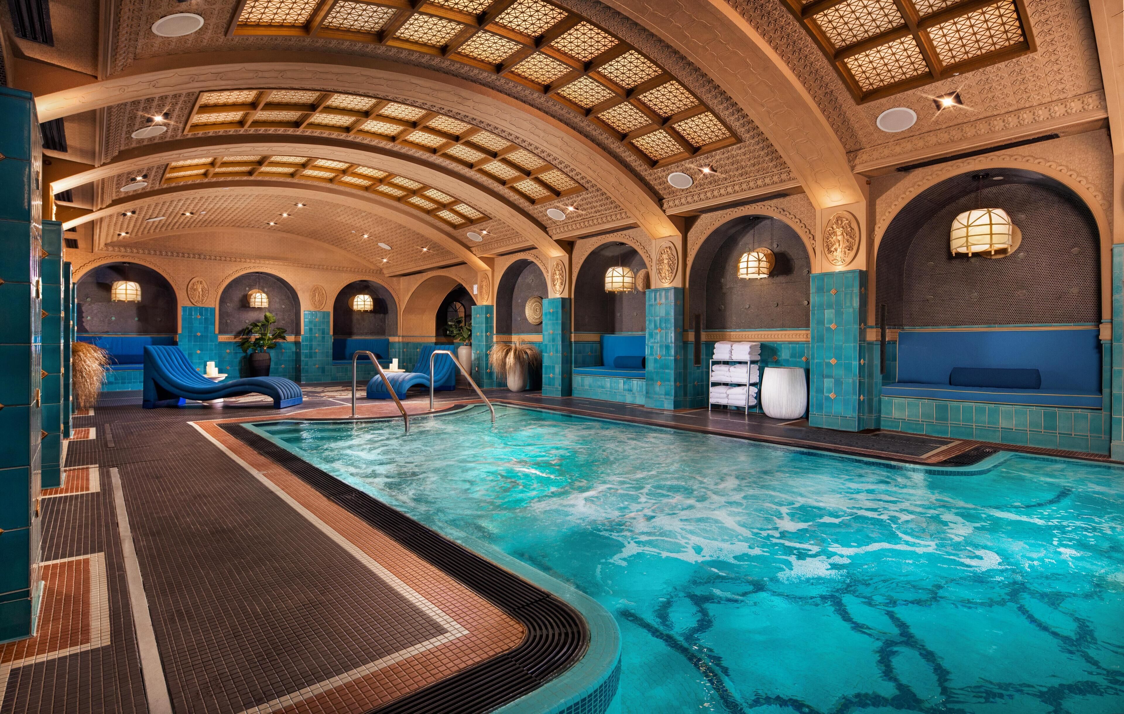 An indoor swimming pool with a tiled floor, arched ceilings, and blue seating areas.