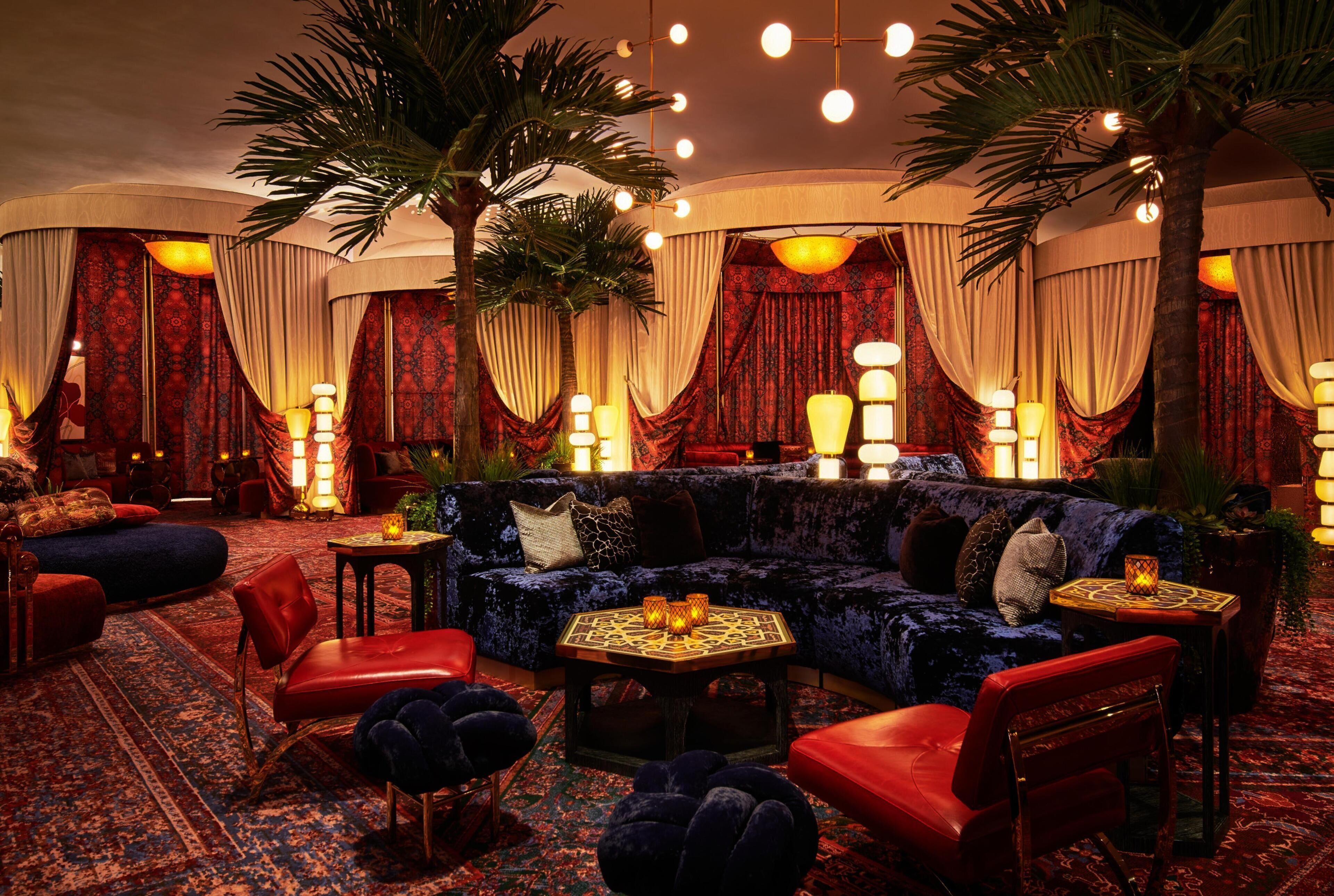 A luxurious lounge area with a plush sofa, red chairs, a patterned rug, and ambient lighting.