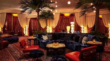 A luxurious lounge area with a plush sofa, red chairs, a patterned rug, and ambient lighting.