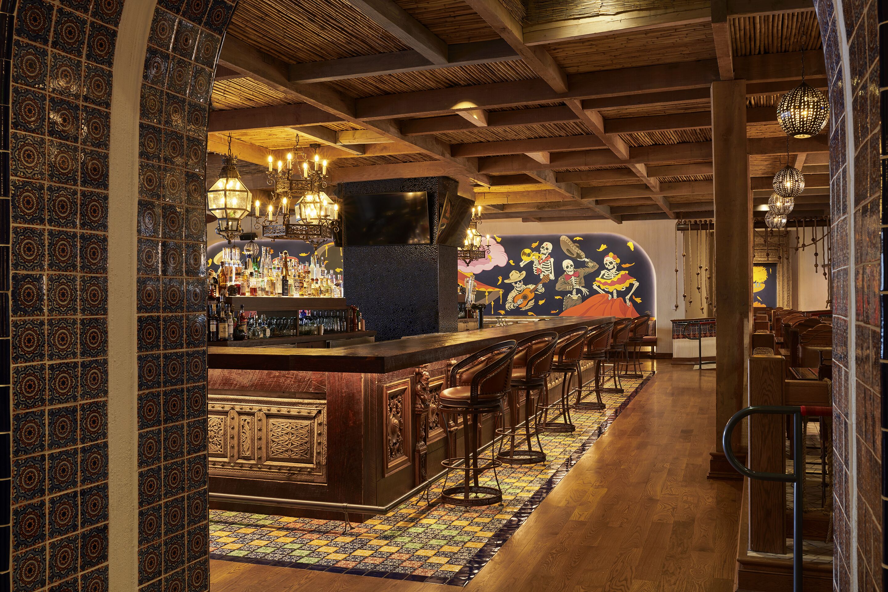 A bar area with a patterned tile wall, wooden ceiling beams, and a tiled floor.
