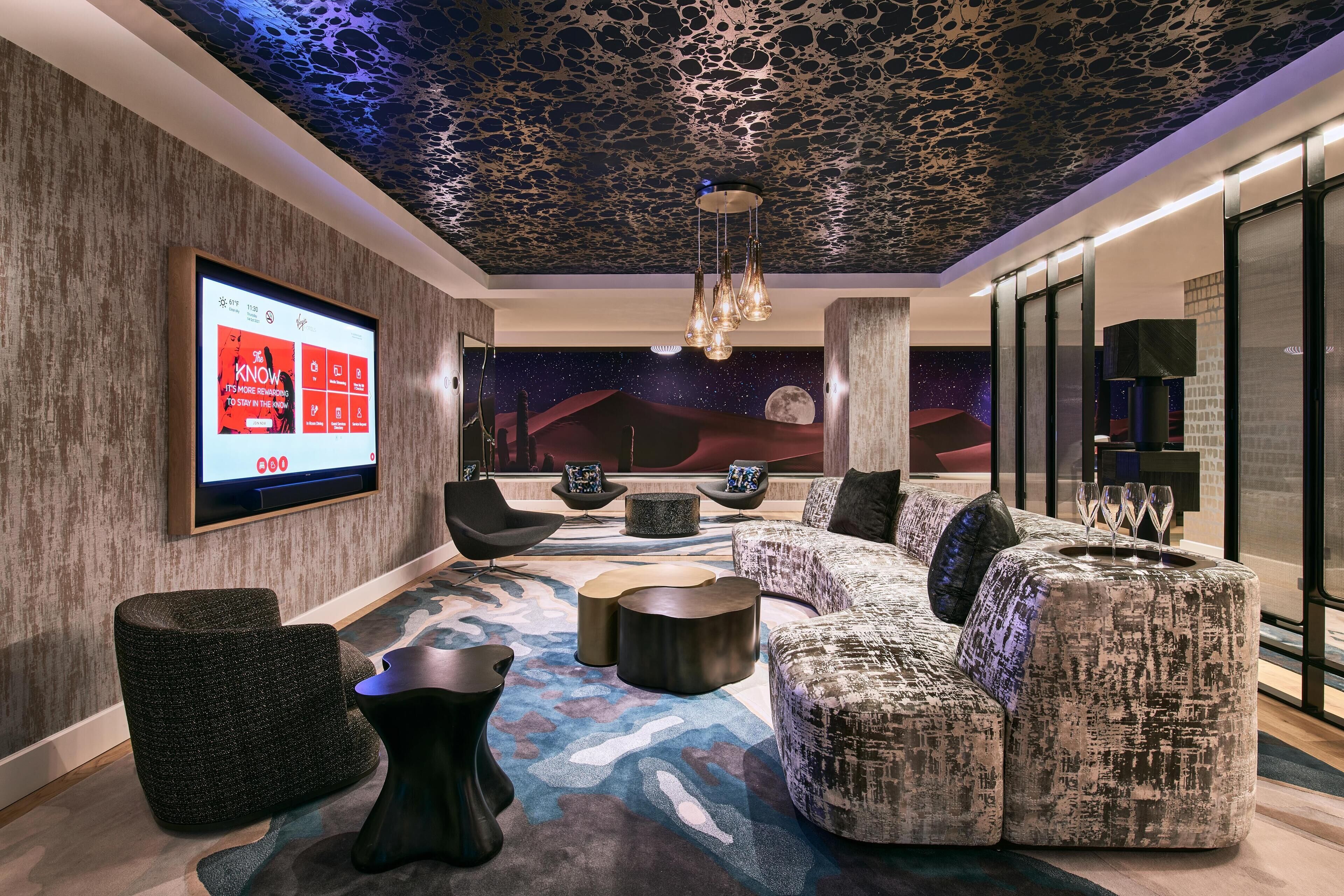 Un espace de détente moderne doté d’un grand écran diffusant un film, de sièges confortables et d’une fresque murale représentant un ciel étoilé.