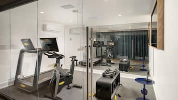 A modern gym with exercise equipment, a mirrored wall, and a small table with a laptop.