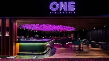 Interior moderno de una parrilla de carne con un llamativo letrero de neón, una zona de bar y un espacio de asientos.