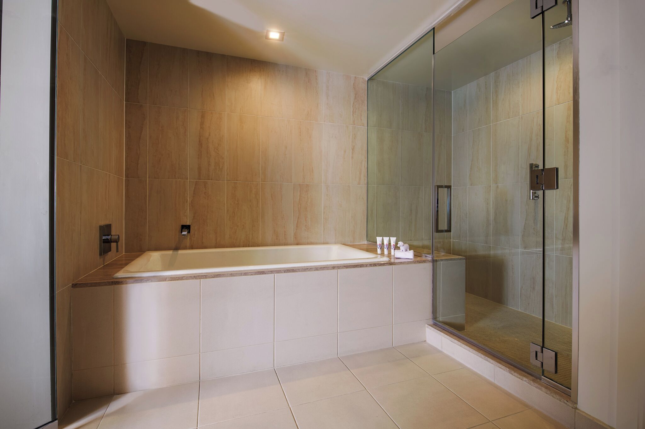 Un baño moderno con una bañera grande, cabina de ducha con mampara de vidrio y suelo de baldosas.