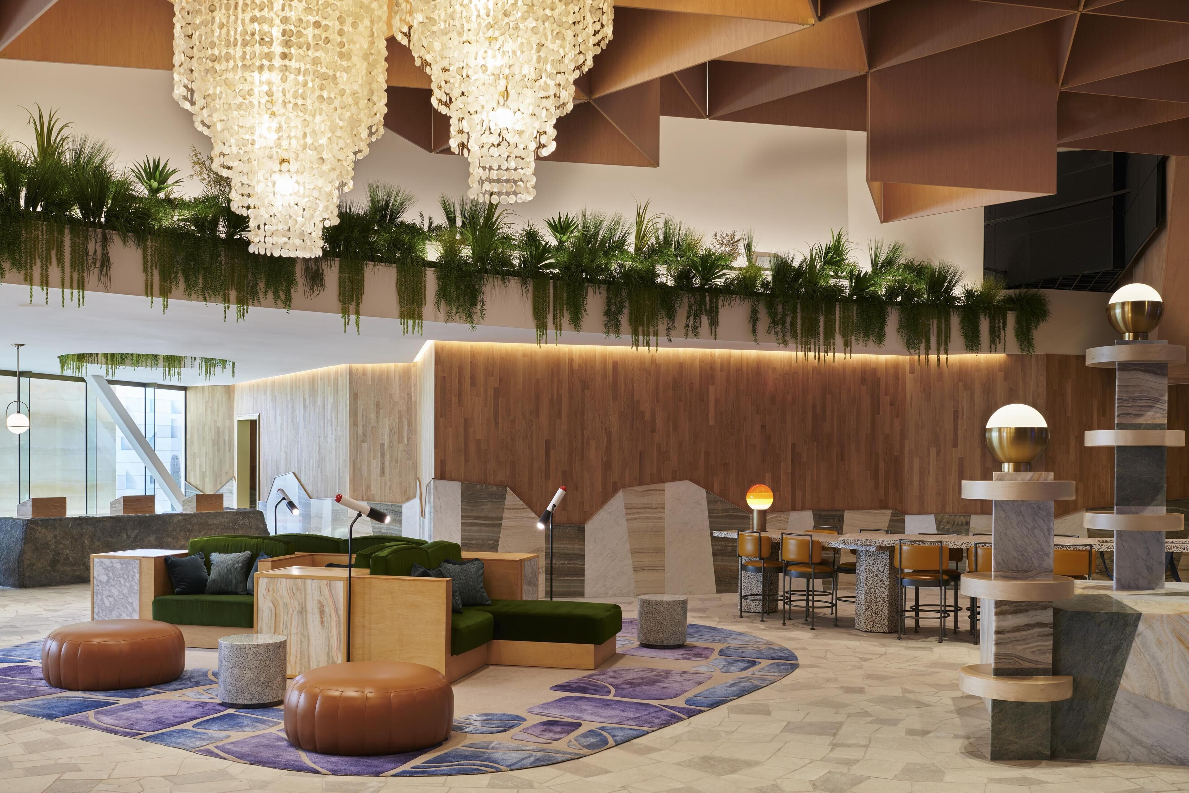 Un vestíbulo moderno con mostrador de recepción de madera, zona de estar con asientos verdes y una lámpara decorativa.