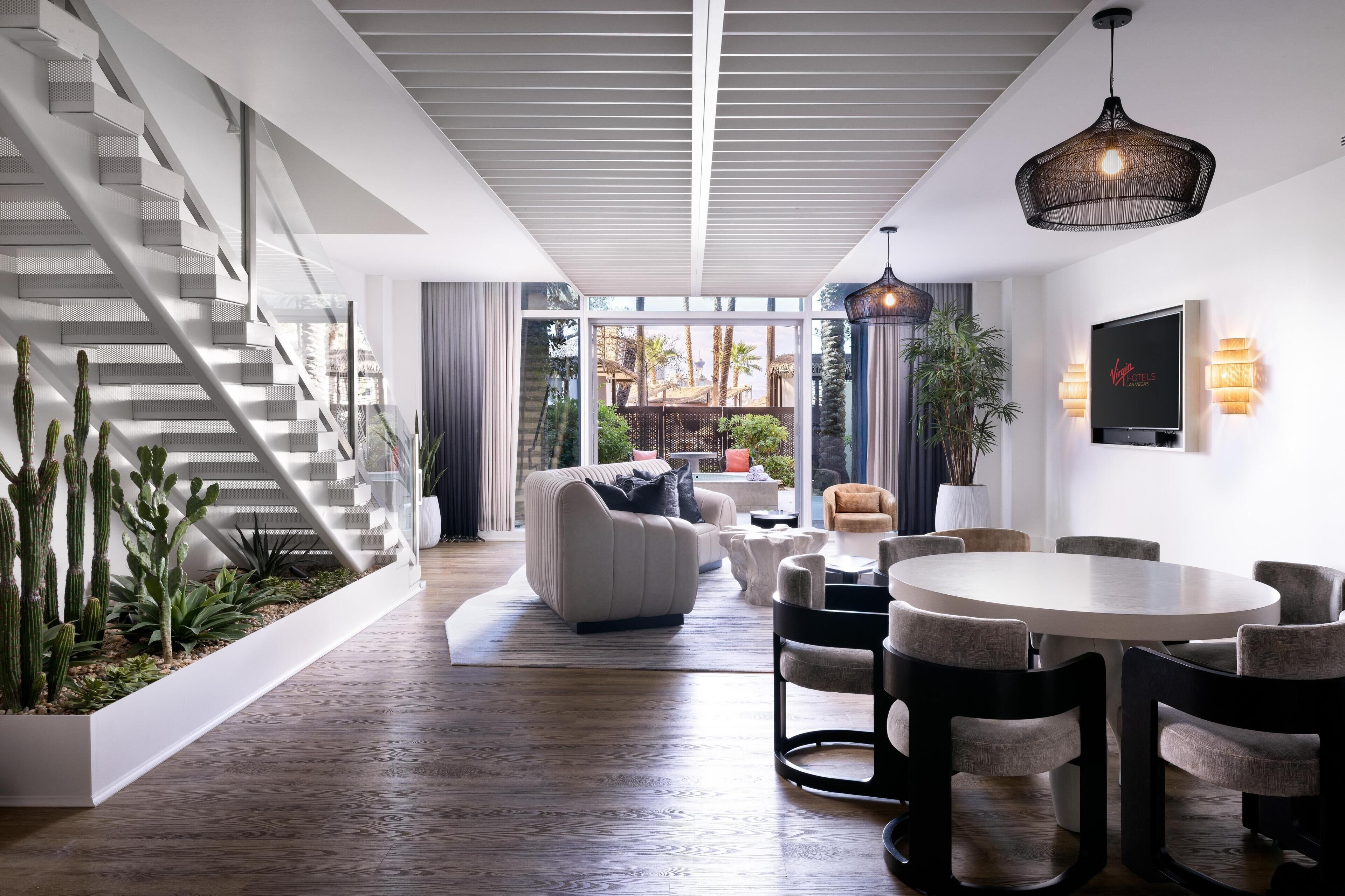 Un interior moderno con una escalera, una sala de estar con sofá y mesa de centro, y un comedor con sillas y mesa.