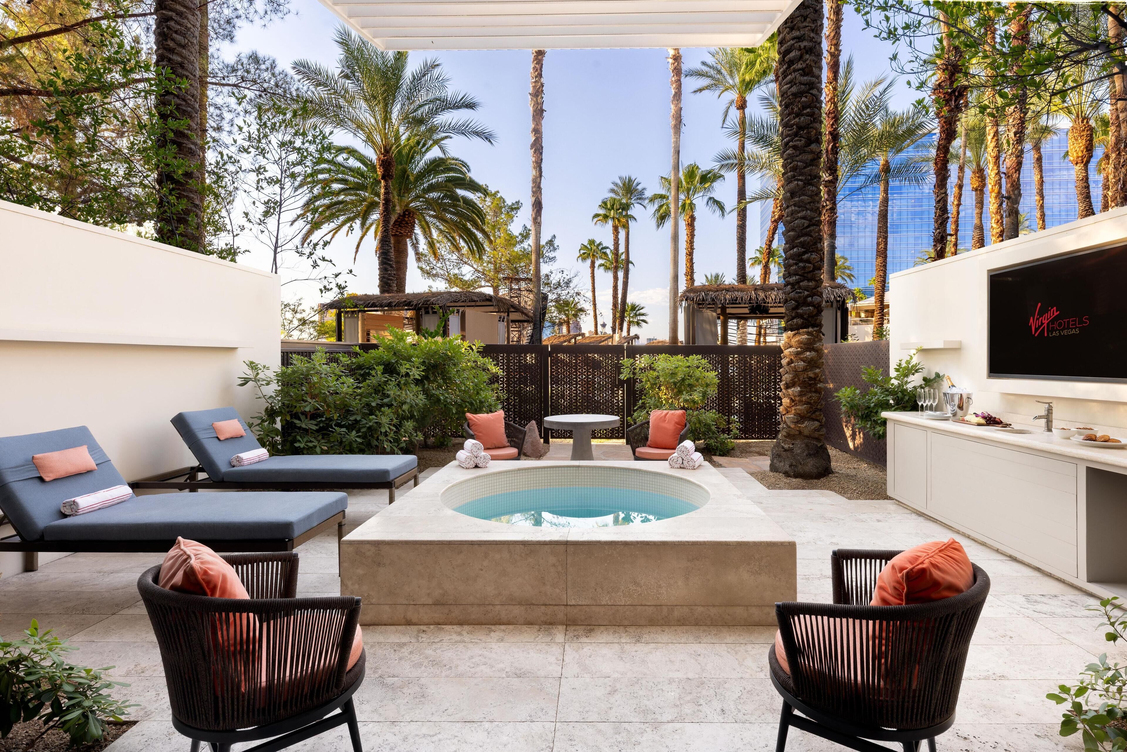 Un área de piscina con sillones de descanso, un jacuzzi y vistas a palmeras y un edificio al fondo.
