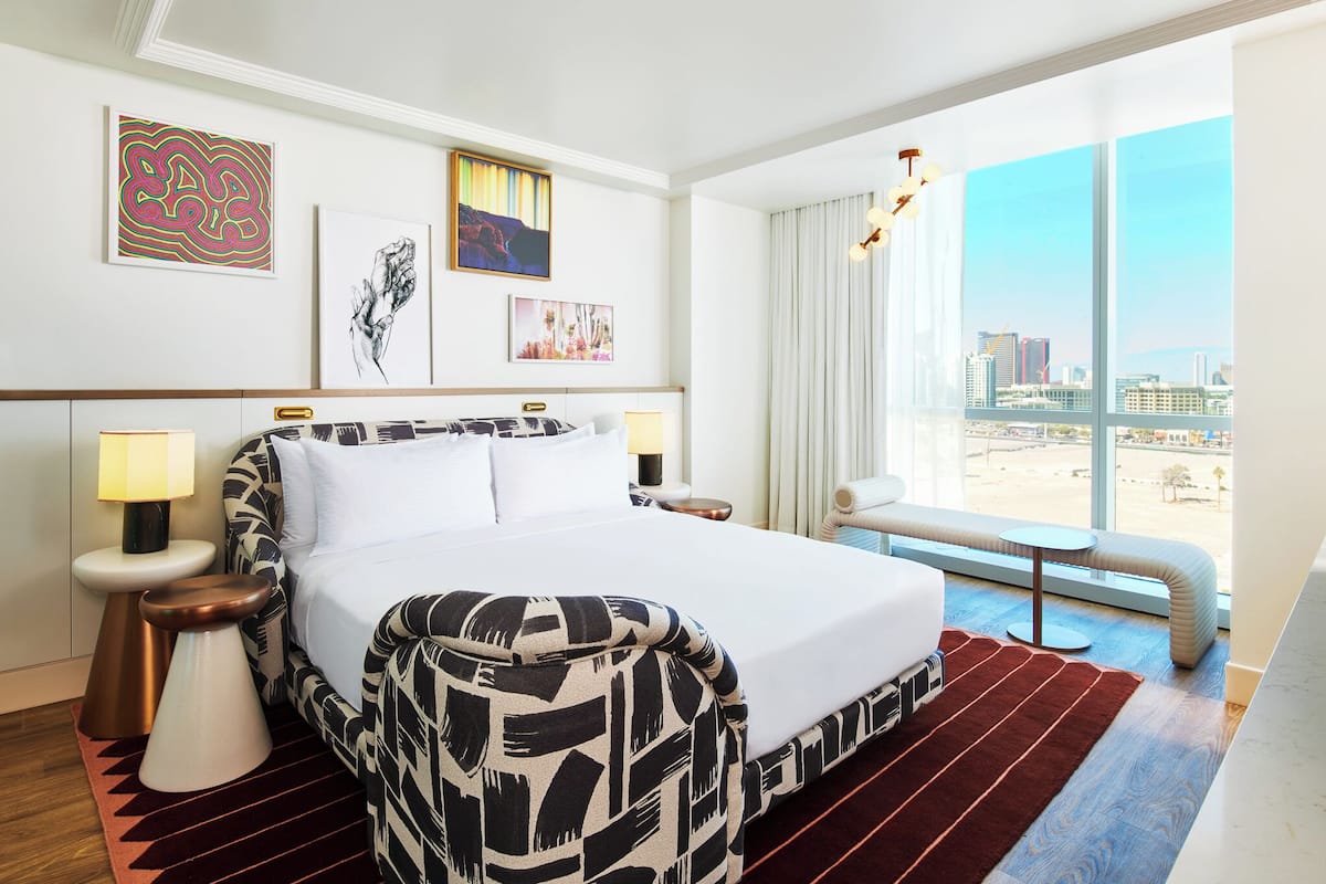 A hotel room with a large bed, a view of the city, and artwork on the walls.
