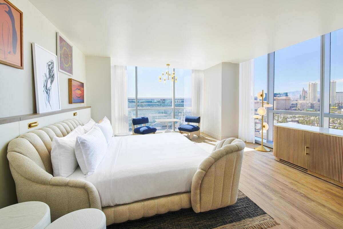 A modern bedroom with a large bed, a view of the city through floor-to-ceiling windows, and a cityscape visible from the window.