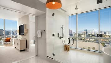 A modern bathroom with a glass shower enclosure, a large window offering a city view, and a minimalist design.