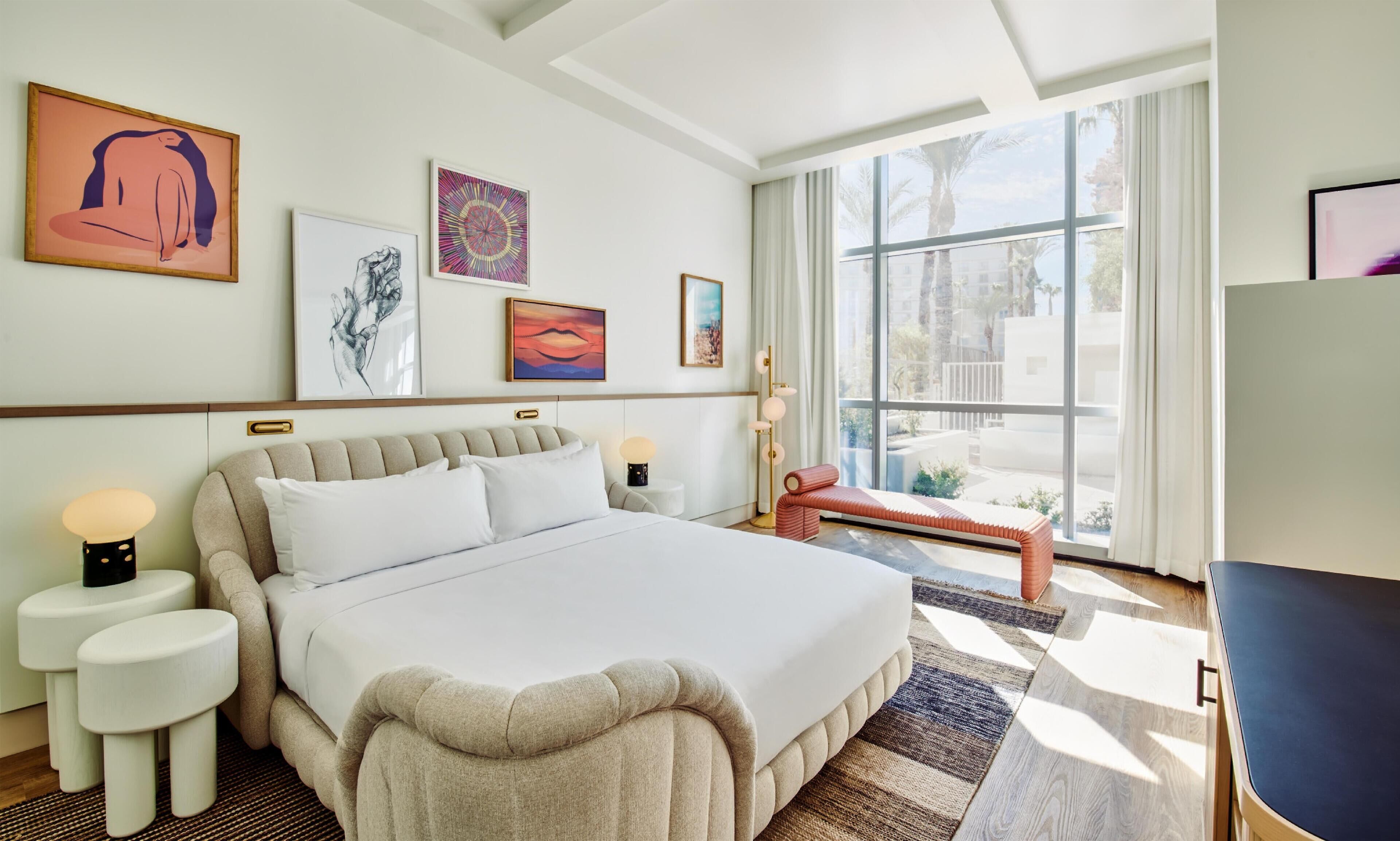 Una habitación de hotel moderna con una cama grande, un banco y obras de arte en las paredes.