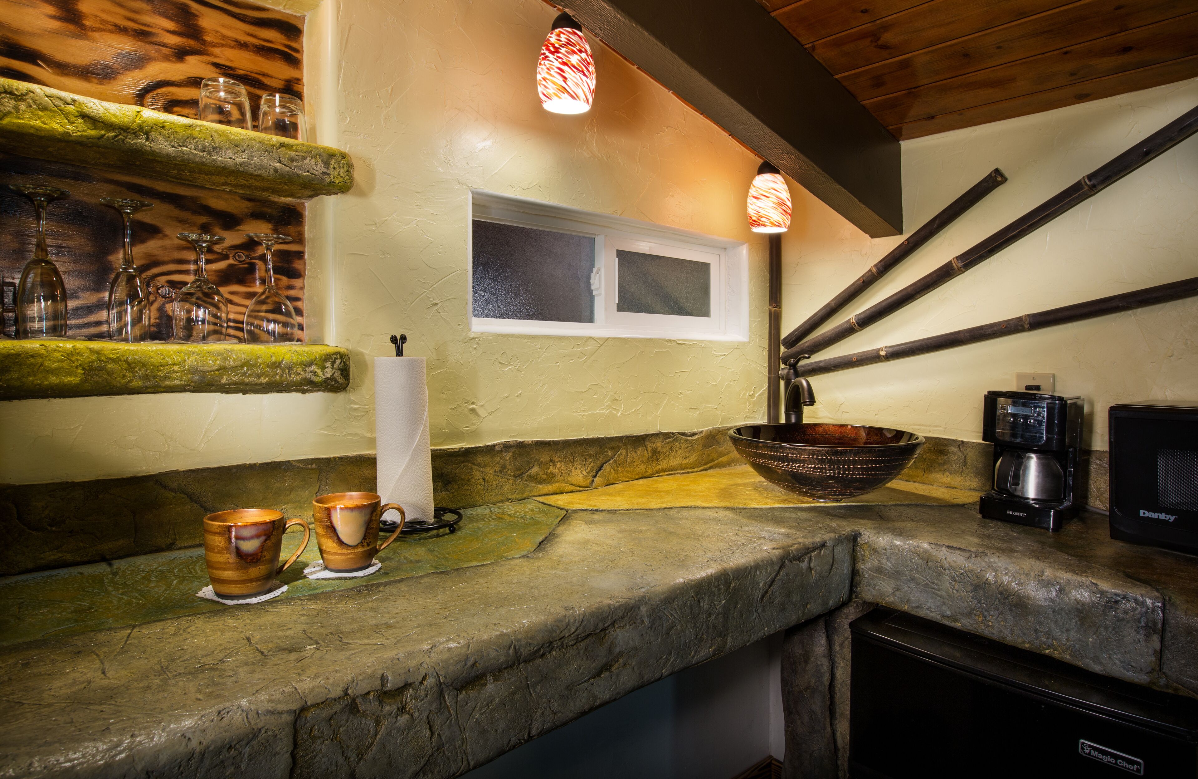 A kitchen with a stone countertop, a window, a coffee maker, and a bowl.