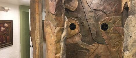 A room with a rock-like wall, a framed picture, and a door.