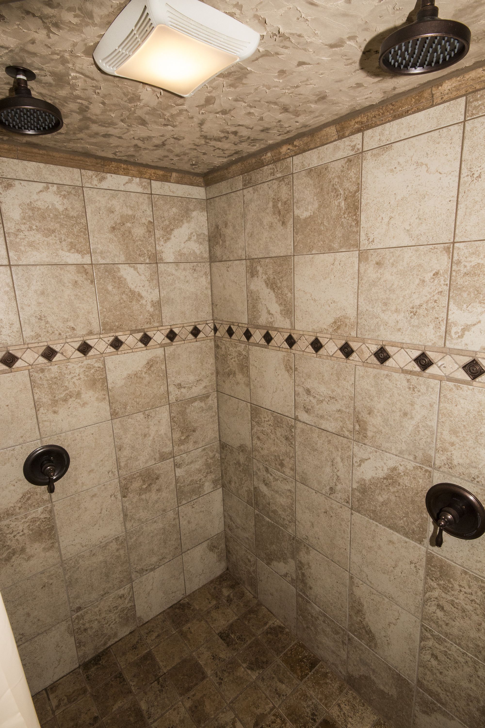 Une zone de douche carrelée, équipée d’un pommeau de douche à main et d’un pommeau de douche fixé au mur.