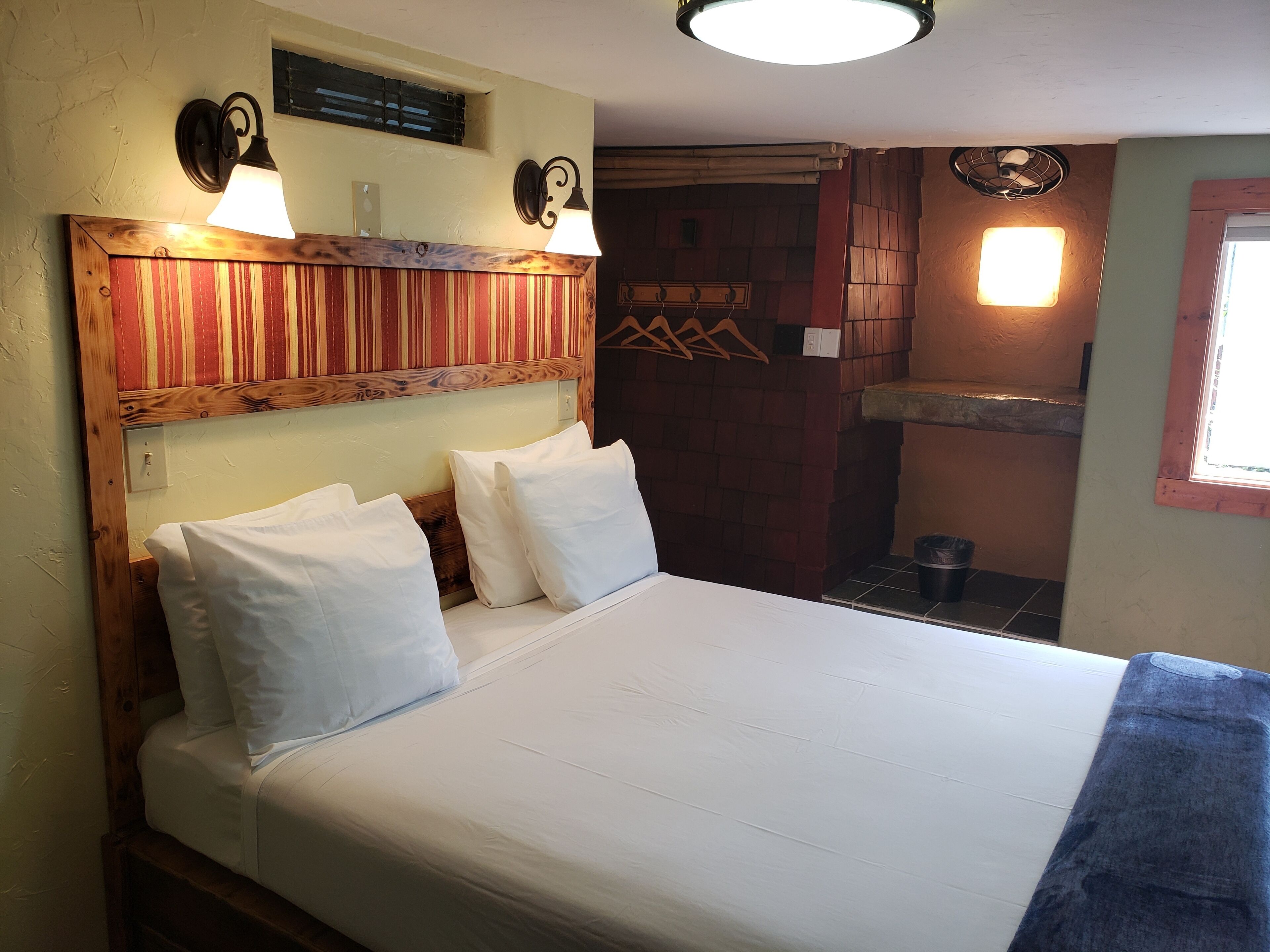 A bed with white linens and pillows, a wooden headboard, and two wall-mounted lamps.