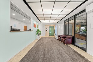 A reception area with a reception desk, a potted plant, a seating area with leather chairs, and a green elevator door. - Chasely Apartment Hotel (Auchenflower)