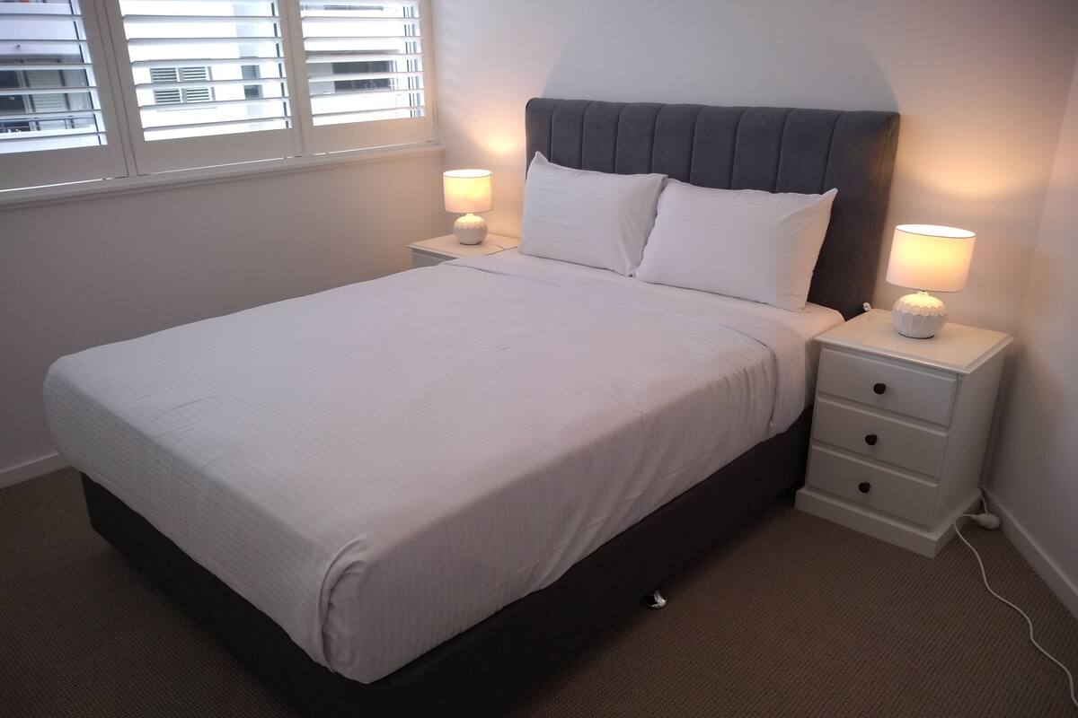 A neatly made bed with white linens, a dark headboard, and two bedside lamps on matching nightstands.