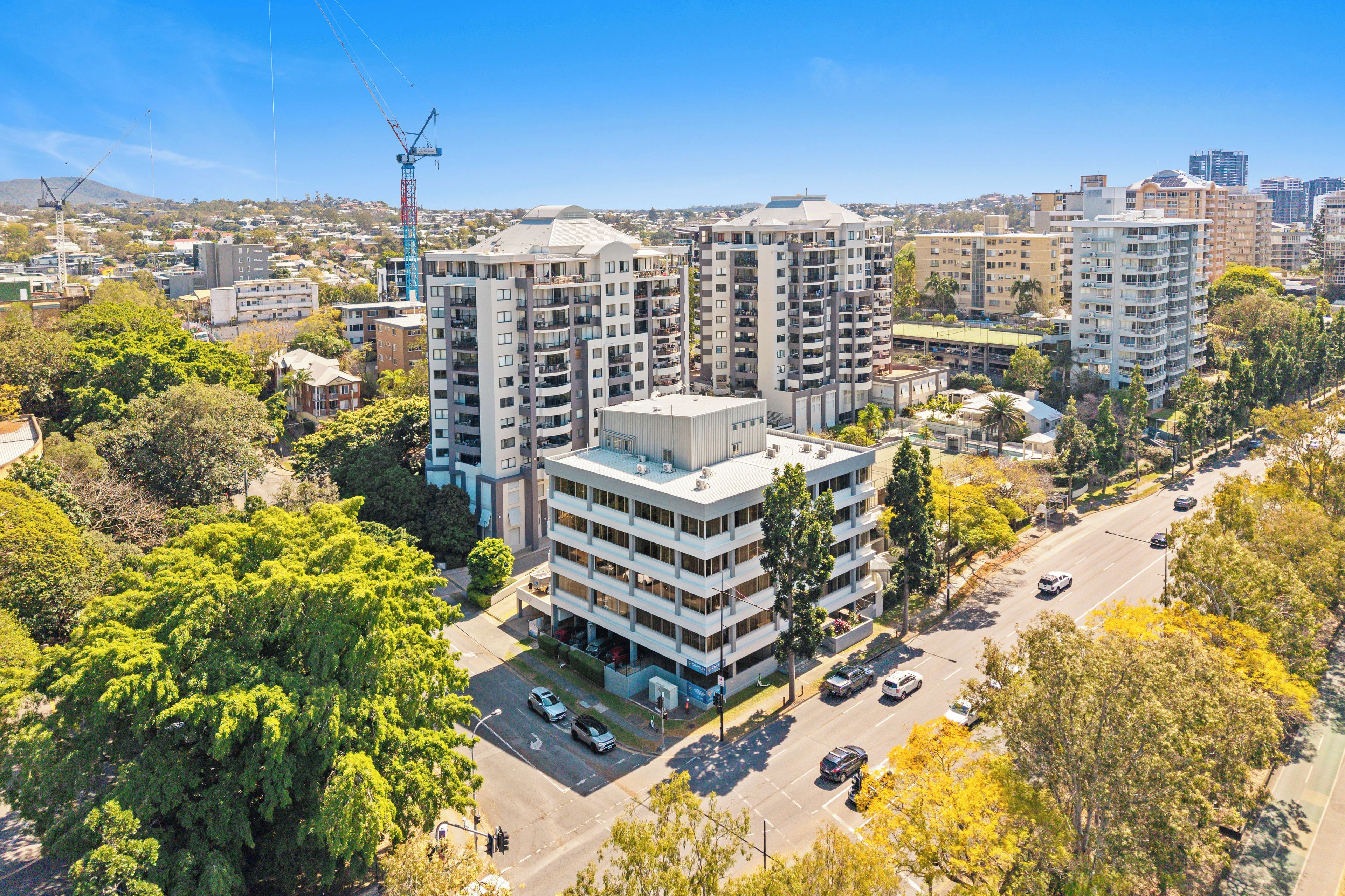 A high-rise residential building with multiple balconies, surrounded by greenery and other buildings.