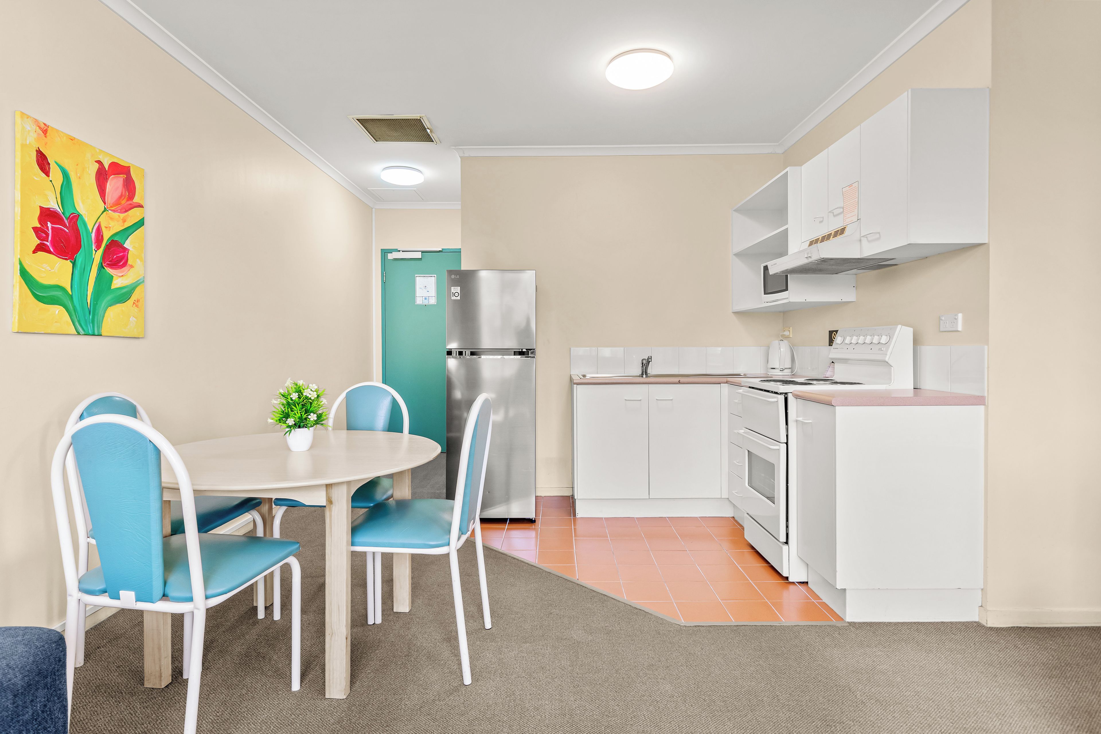 A compact kitchen with a dining area, white cabinetry, a stainless steel refrigerator, and a small table with chairs.