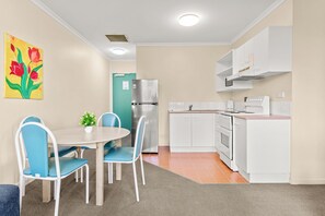 A compact kitchen with a dining area, white cabinetry, a stainless steel refrigerator, and a small table with chairs.