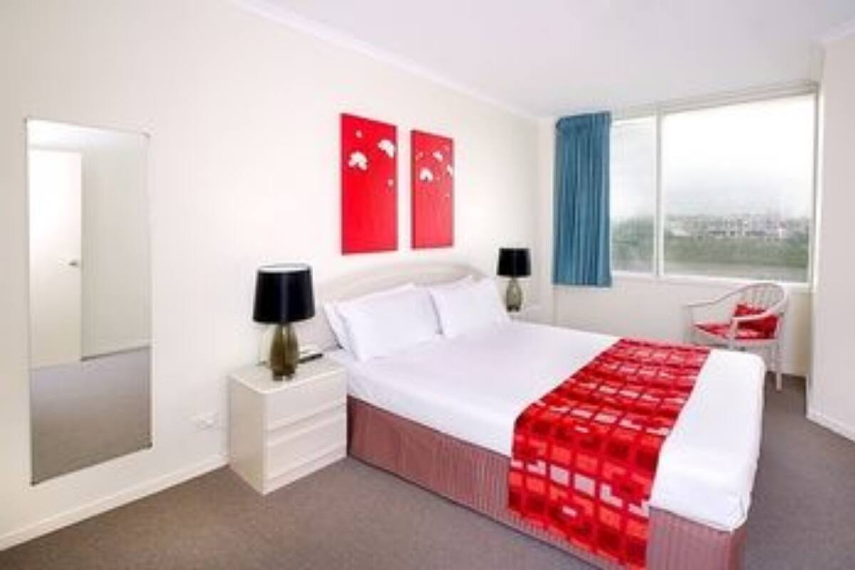 A hotel room with a bed, bedside tables, a window with a view, and red artwork on the wall.