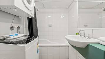 Ein kleines Badezimmer mit Waschmaschine, Badewanne und Waschbecken.