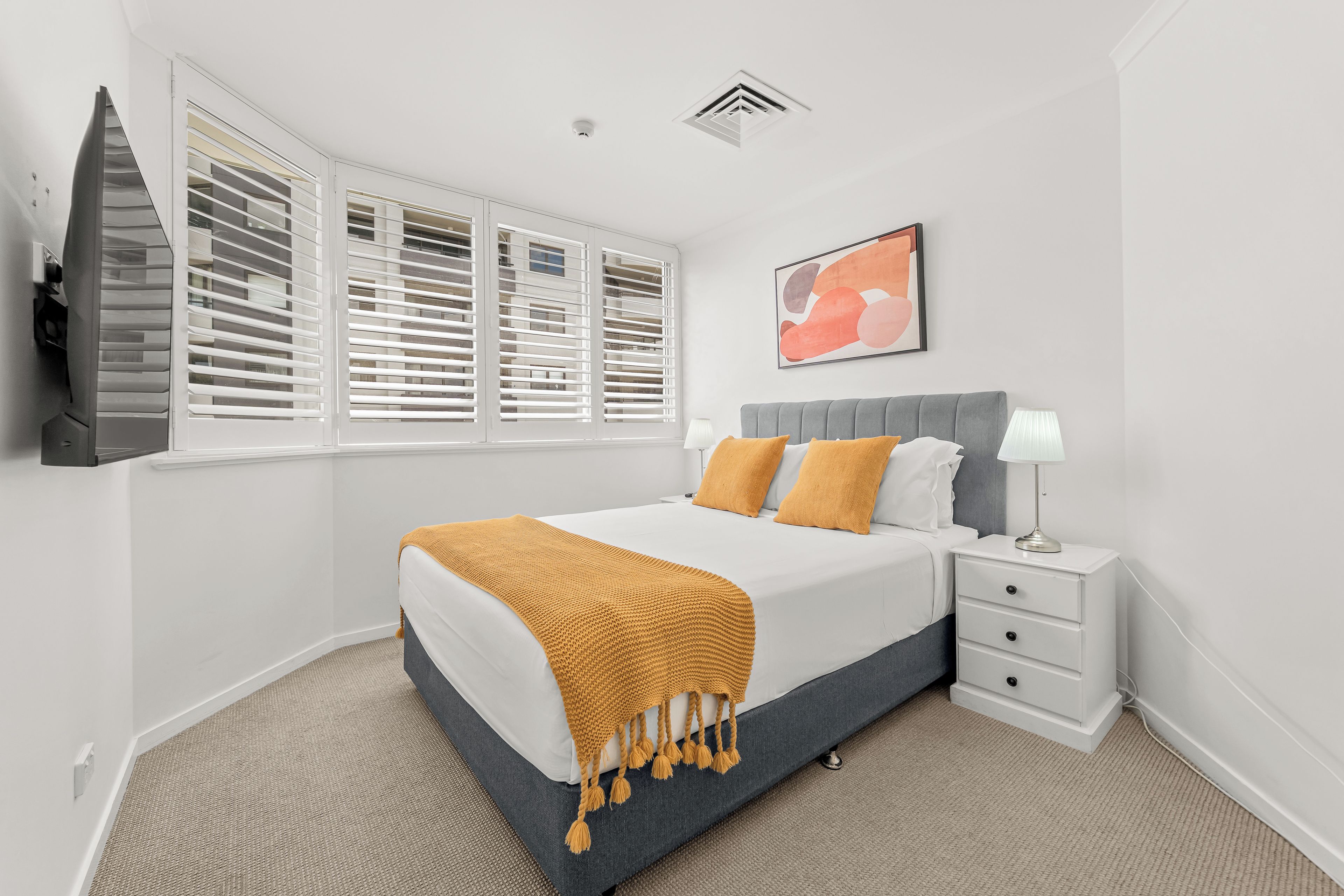 A bedroom with a bed, bedside table, lamp, and a window with blinds.