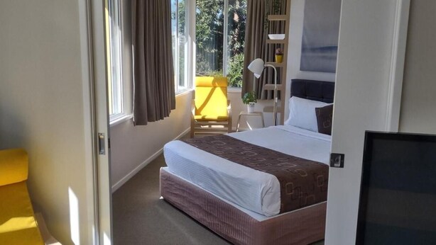 A hotel room with a bed, a chair, a desk, and a window with curtains. - Chasely Apartment Hotel (Auchenflower)