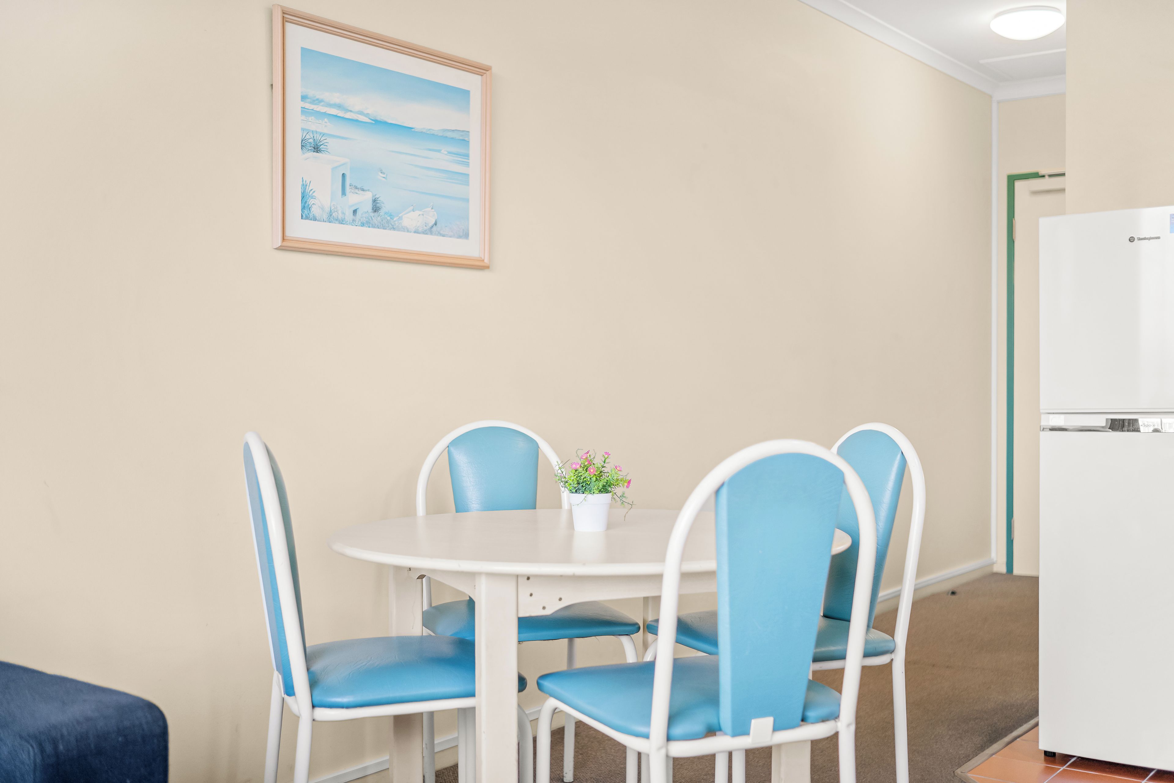 A dining area with a round table, four chairs, a small potted plant, and a framed picture on the wall.