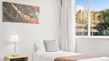 Una camera da letto con un letto, un comodino, una lampada, una finestra con tende e un quadro astratto appeso al muro.
